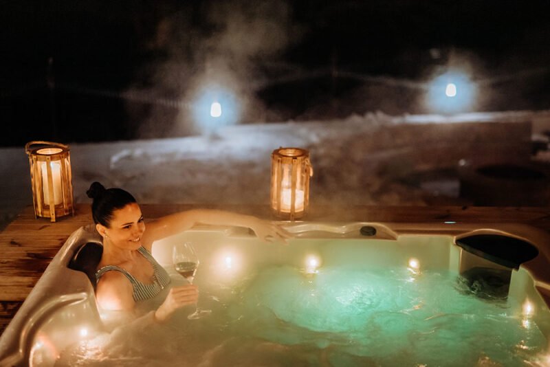 young woman enjoying outdoor bathtub in her terrace during cold winter evening.