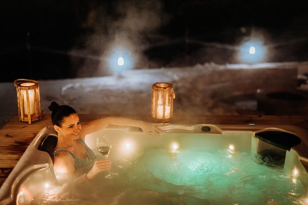 young woman enjoying outdoor bathtub in her terrace during cold winter evening.