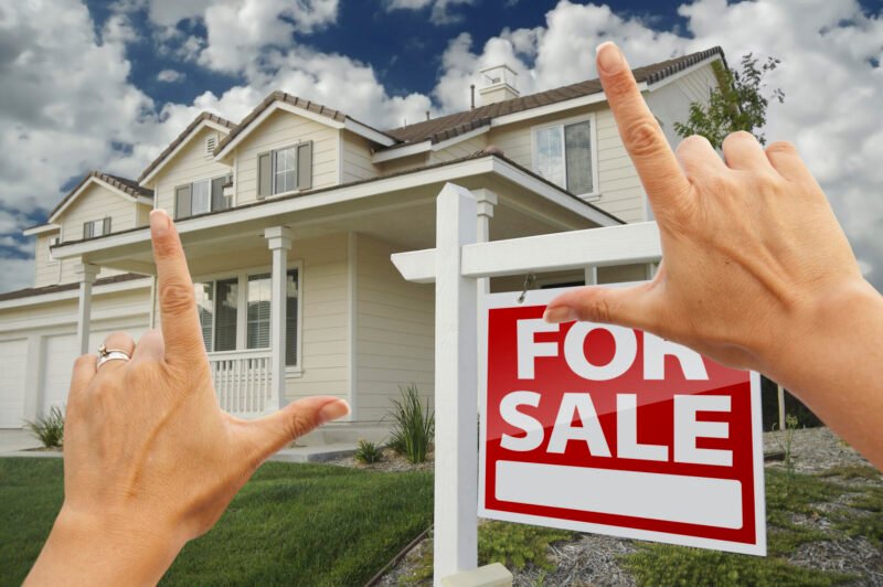 female hands framing home for sale real estate sign in front of new house.